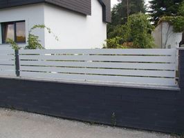 Zaun ums Grundstück mit dunkler Betonmauer und oben mit weißen Latten